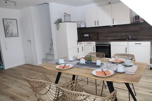 Une cuisine moderne avec des meubles blancs, un plan de travail foncé et une table à manger en bois pour quatre personnes.