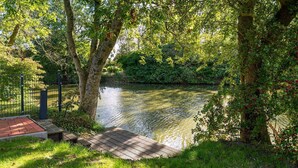 A riverside walkway with a wooden deck, surrounded by trees and greenery.