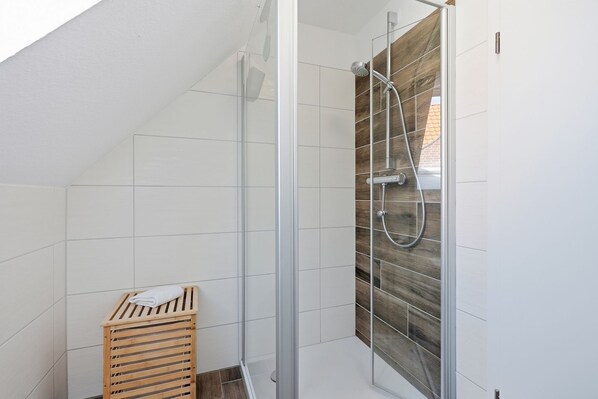 Una ducha con puerta de vidrio, paredes de azulejos blancos y un banco de madera con listones.