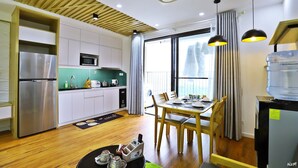Cozinha moderna com micro-ondas embutido, frigorífico em aço inoxidável e armários de madeira. Possui um espaço de jantar com mesa e cadeiras, e uma janela grande que oferece vista para o exterior.