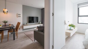 Uma sala de estar moderna com sofá, mesa de jantar com cadeiras, TV fixada na parede e janela com vista para a cidade.