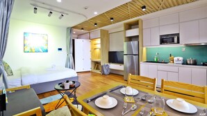 Quarto de hotel moderno com uma cama, área de jantar com uma mesa posta para dois, cozinha com micro-ondas e uma televisão.