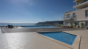Ein Poolbereich auf dem Dach mit zwei Pools, Liegestühlen und Meerblick.