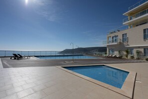 Un espace piscine sur le toit, comprenant deux piscines, des chaises longues et une vue sur la mer.