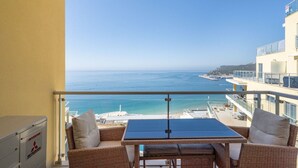 Ein Balkon mit Tisch und Stühlen, der Blick auf die Küste mit Gebäuden und dem Meer bietet.