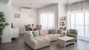 Ein modernes Wohnzimmer mit einer Eckcouch, einem Couchtisch, einem Essbereich mit Tisch und Stühlen sowie einem Bücherregal.