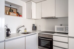 Cozinha moderna com armários brancos, micro-ondas embutido, pia de aço inoxidável e máquina de café.