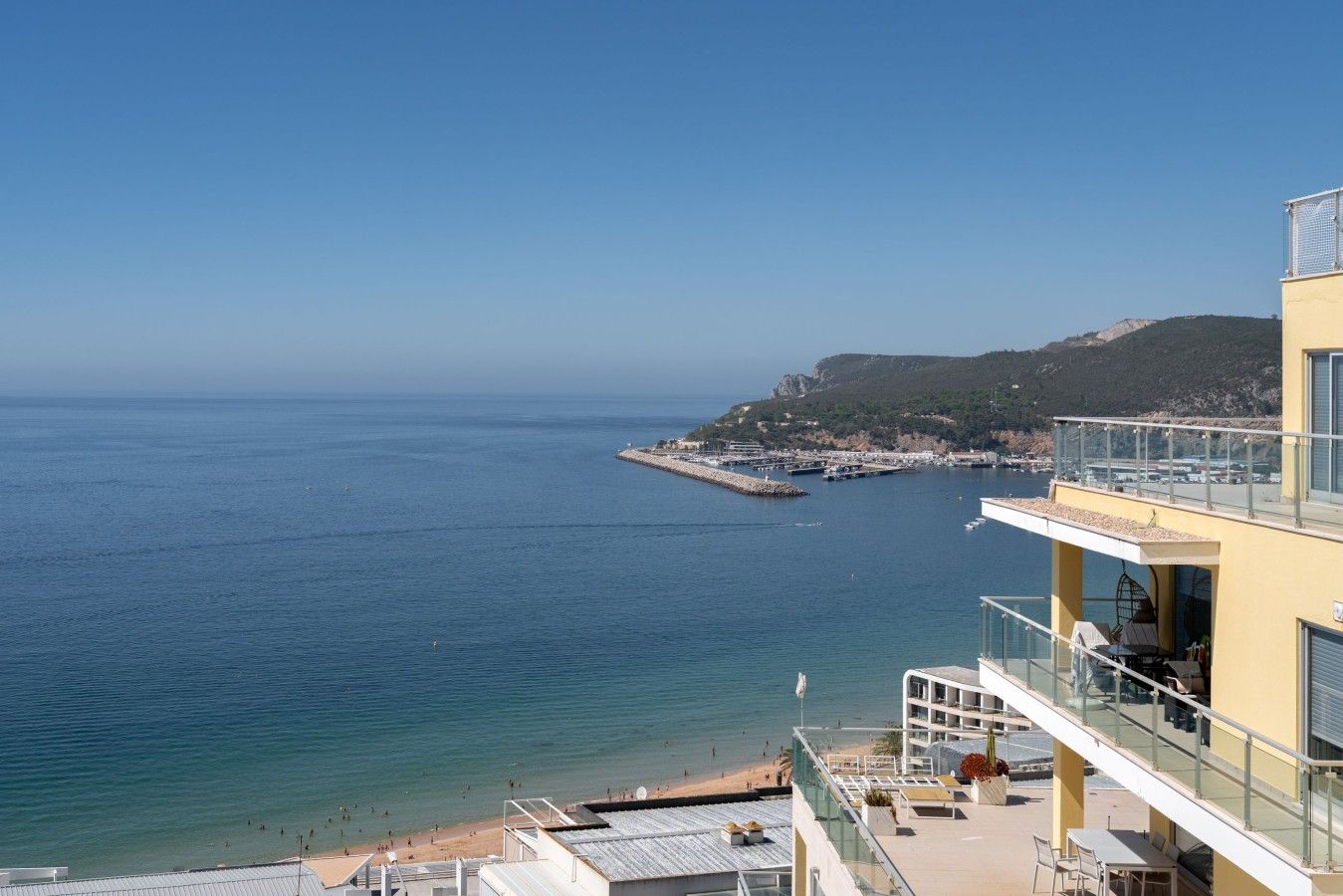 Un hôtel situé sur la côte, doté d’un balcon offrant une vue sur la mer, une plage et un promontoire rocheux au loin.