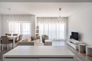 A modern living room with a sofa, TV, and dining area. - Janelas de Zimbra Lovely Apt with Pool and Sea View by Lisbeyond (Sesimbra)