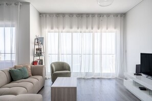 Ein modernes Wohnzimmer mit einer Couch, einem Sessel, einem Couchtisch, einem Fernseher und einem Bücherregal.