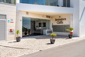Ein Hotel Eingang mit Glastür, Blumentöpfen und einem Schild mit der Aufschrift 'Sesimbra Cliffs'.