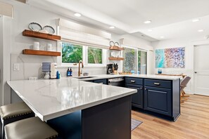 Een moderne keuken met een groot eiland, donkere kastjes en uitzicht op de omgeving door grote ramen.