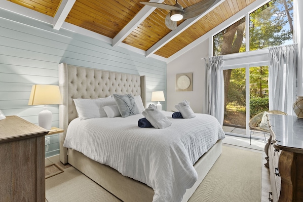 A bedroom with a large bed, a wooden ceiling, and a view of the outdoors.