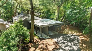 A modern cabin with a large deck, surrounded by dense forest.