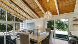 Een modern interieur met een houten plafond, grote ramen, een eethoek en uitzicht op groen.