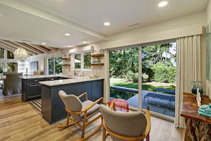 A modern kitchen with a central island, wooden chairs, and a view of a backyard with a pool.