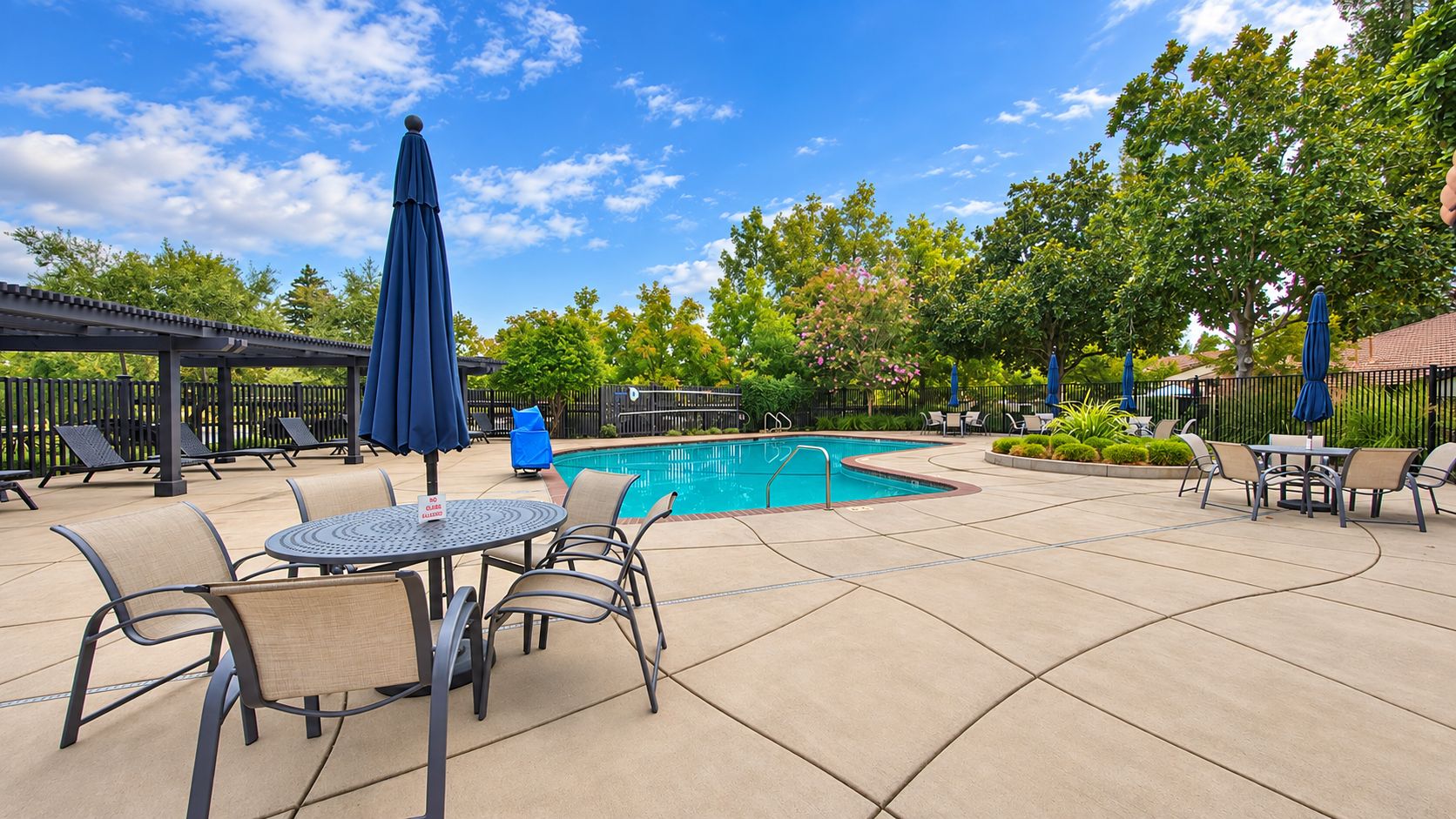 An outdoor pool area with lounge chairs, a table, and umbrellas.