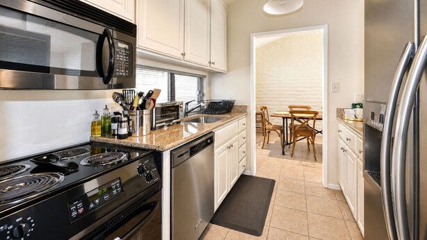 A modern kitchen with stainless steel appliances, white cabinetry, and a dining area with wooden chairs. - Spacious 3BR, Golf course views, BBQ, pool at Silverado (Napa)