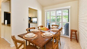 A dining area with a wooden table set for four, surrounded by chairs, with a view of the outdoors through large windows. - Spacious 3BR, Golf course views, BBQ, pool at Silverado (Napa)
