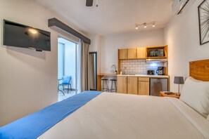 A hotel room with a bed, a TV, a kitchenette, and a small dining area.