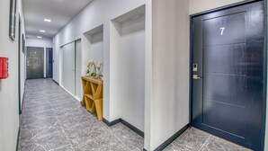 A hallway with a dark door marked with the number 7, a wooden shelf with a plant, and a tiled floor. - Stylish Downtown Studio Apartment with Patio & A/C! (San jose)