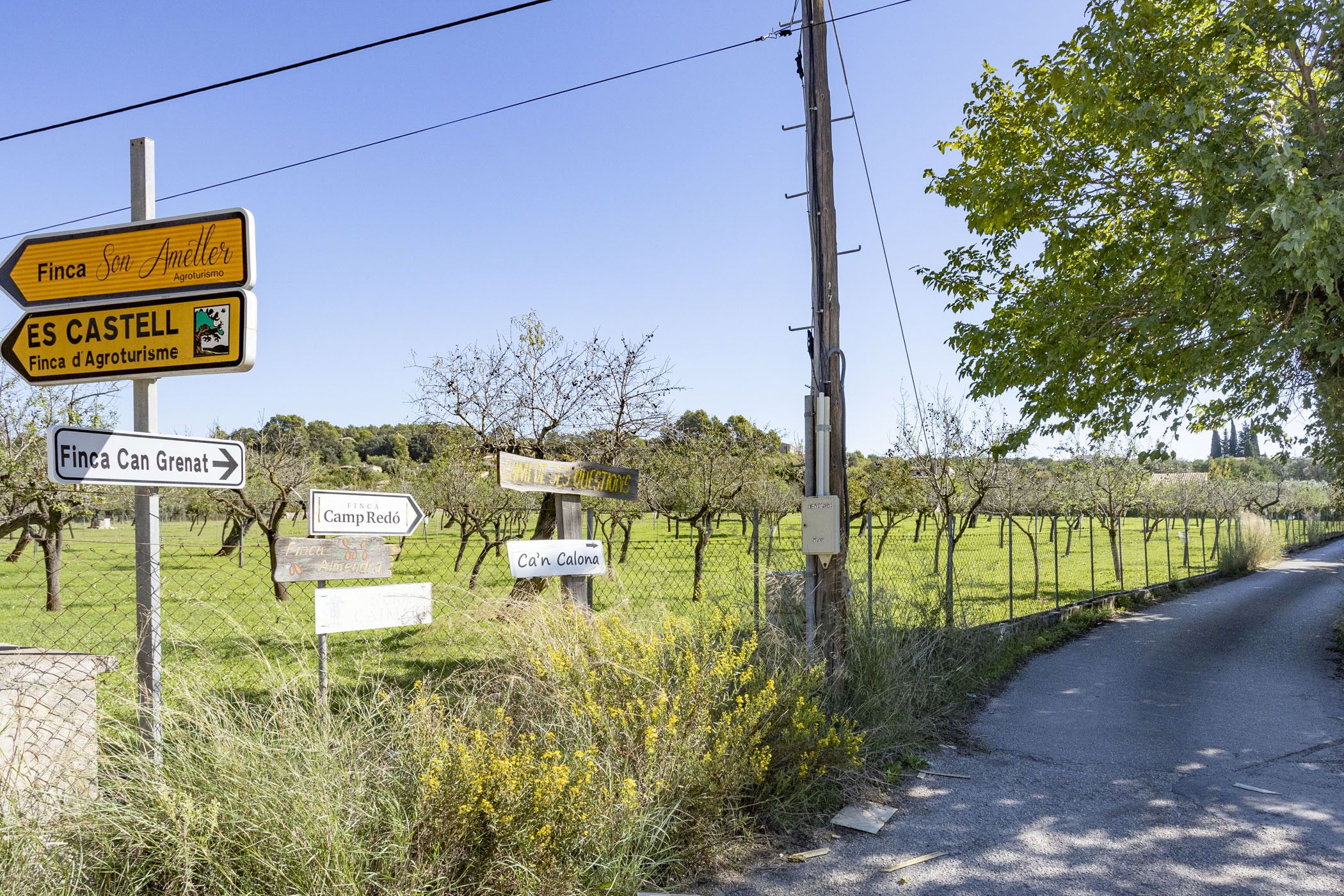 Een landweg met richtingaanwijzingen naar verschillende locaties, zoals Finca San Ameller, ES CASTELL en Finca Can Grenat.