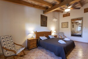 Une chambre à coucher avec un lit doté d’une tête de lit en bois, deux tables de chevet avec des lampes, un fauteuil à bascule et un grand miroir au mur.