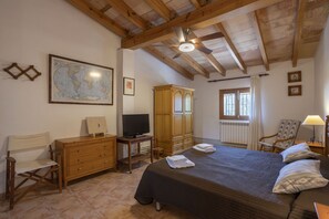 Une chambre avec un grand lit, une armoire en bois, un bureau avec une télévision, une carte accrochée au mur et une fenêtre avec des rideaux.