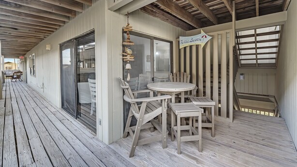Et overdækket udendørsareal med træterrasse, en glasdør og et skilt med teksten "To the Beach".