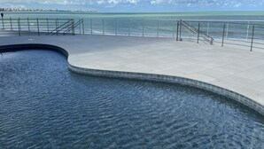 Une piscine à bord incurvé, dotée d’une terrasse carrelée et d’un garde-corps donnant sur une étendue d’eau.