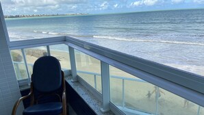 Un balcon avec vue sur l’océan et la plage, une chaise et un sol carrelé.
