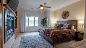 Un dormitorio con una cama grande, ventilador de techo, televisor y vistas al exterior.