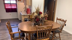 Un coin repas avec une table ronde en bois, entourée de quatre chaises en bois dotées d’assises rembourrées. Un vase contenant des fleurs séchées est posé sur la table.