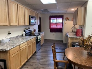 A compact kitchen with wooden cabinets, a built-in microwave, a stove, and a dining area with a wooden table and chairs. - The Eagle's Nest is an oilfield building converted into a beautiful house right on the river. (Thermopolis)