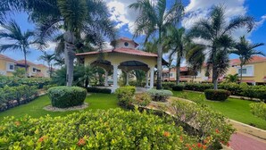 Un jardín bien cuidado con un pabellón, palmeras y setos ordenados.