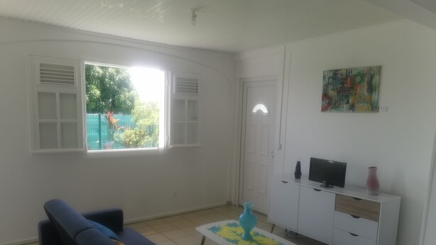 Ein Wohnzimmer mit einer Couch, einem Couchtisch, einem Fernseher auf einem Schrank und einem Fenster mit Jalousien.