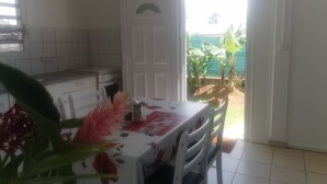 Eine Küche mit weißen Schränken, einer gefliesten Spritzschutzleiste und einem Fenster. Ein Tisch mit einer blumigen Tischdecke und Stühlen steht dort.