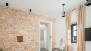A bedroom with a stone wall, a bed, a desk with a mirror, and a window with curtains.