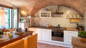 A kitchen with white cabinets, a stone arch ceiling, a gas stove, and a window with a view of greenery. - Nice apartment for 6 guests with terrace and pets allowed (Dolcedo)