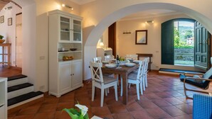 A dining area with a table set for six, white chairs, a cabinet with glass doors, and a view through an open door. - Nice apartment for 6 guests with terrace and pets allowed (Dolcedo)