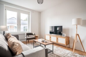A modern living room with a sofa, armchair, coffee table, TV, and floor lamp. - Bright Horgen 2.5 Room w/ Storage, 3 min to Market, by Blueground (Zurich)