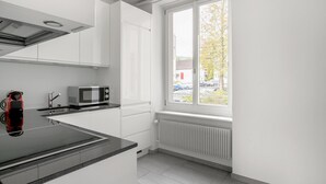 A modern kitchen with white cabinets, a black countertop, a microwave, and a window with a view of parked cars and trees. - Bright Horgen 2.5 Room w/ Storage, 3 min to Market, by Blueground (Zurich)