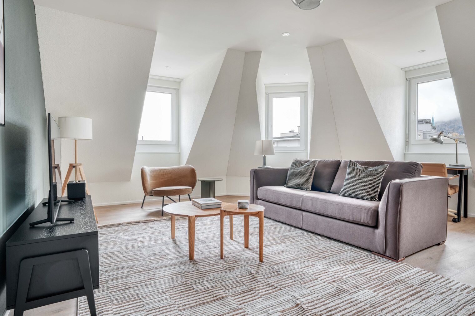 A modern loft apartment with a high ceiling, a grey sofa, a wooden coffee table, and a television on a black stand.