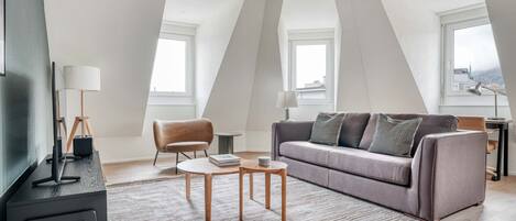 A modern loft apartment with a high ceiling, a grey sofa, a wooden coffee table, and a television on a black stand.