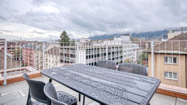 Una terraza en la azotea con mesa y sillas, con vistas a un paisaje urbano que incluye edificios y montañas al fondo.