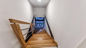 Un escalier étroit avec des marches en bois et des rampes en métal, menant à une fenêtre donnant sur l’extérieur.