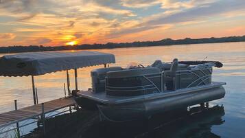 A pontoon boat docked at a pier with a covered seating area and a canopy.