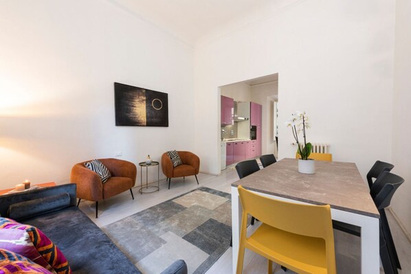 Ein modernes Wohnzimmer mit einer Couch, Sesseln, einem Esstisch und einer Küche im Hintergrund.