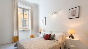 A bedroom with a bed, bedside lamps, a window with curtains, and wall-mounted artwork. - Apartments Florence- Pellicceria Dx (Firenze)