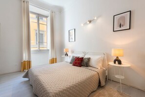 Ein Schlafzimmer mit Bett, Nachttischlampen, einem Fenster mit Vorhängen und Wandbildern.